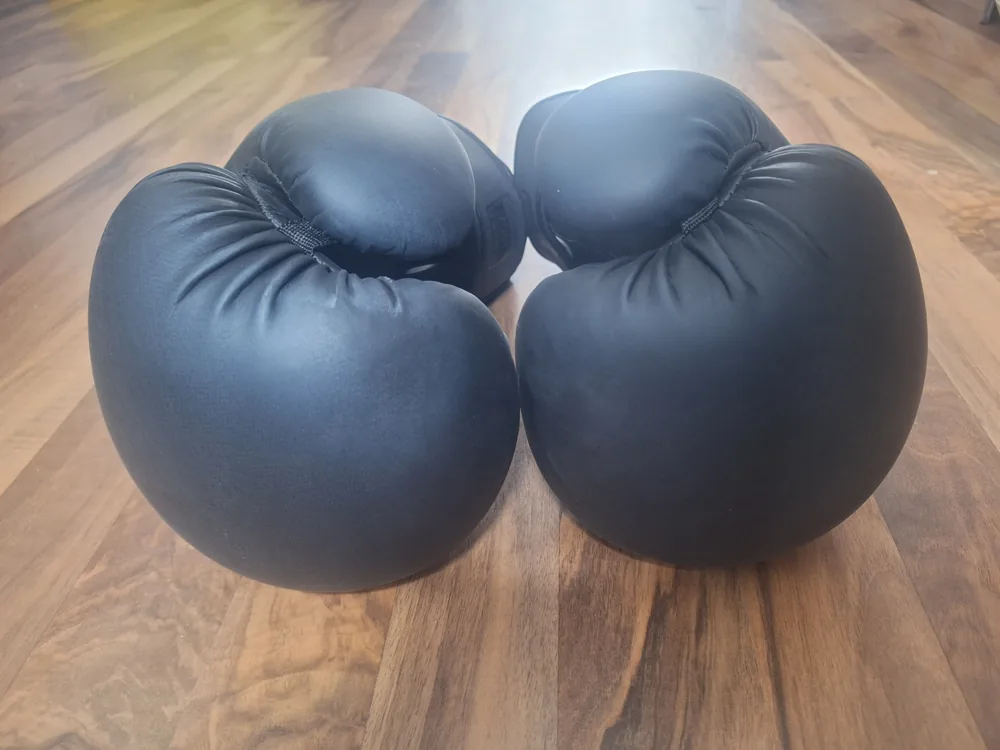 Zwei schwarze Boxhandschuhe auf Holzboden, Trefferflächen zur Kamera